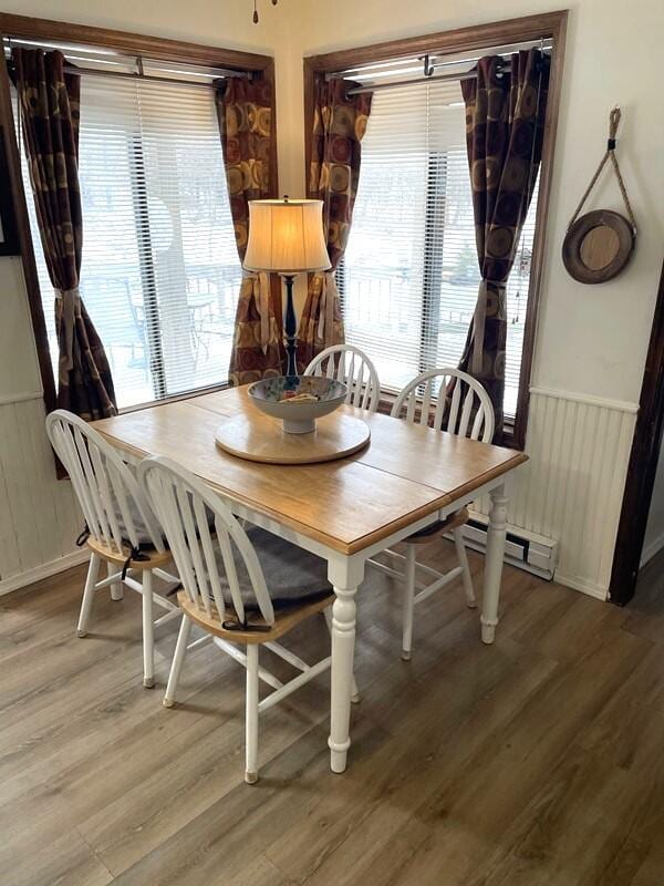 dining room with a wainscoted wall, a baseboard heating unit, and light wood finished floors