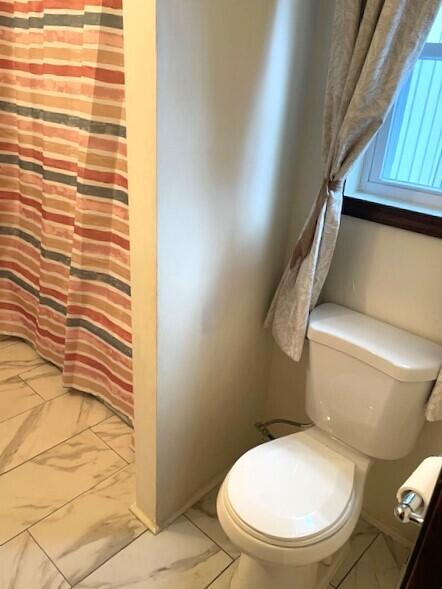 full bathroom with toilet, marble finish floor, and a shower with curtain