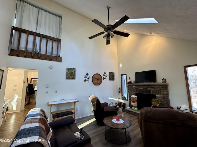 living room featuring a skylight, a ceiling fan, wood finished floors, a brick fireplace, and high vaulted ceiling