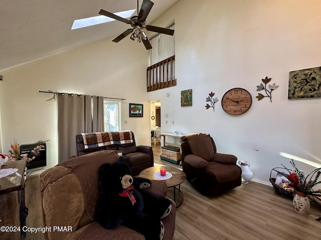 living room featuring high vaulted ceiling, a skylight, wood finished floors, a ceiling fan, and baseboards