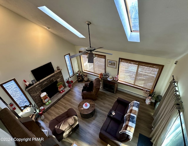 living room with a fireplace, a baseboard radiator, lofted ceiling with skylight, a ceiling fan, and wood finished floors