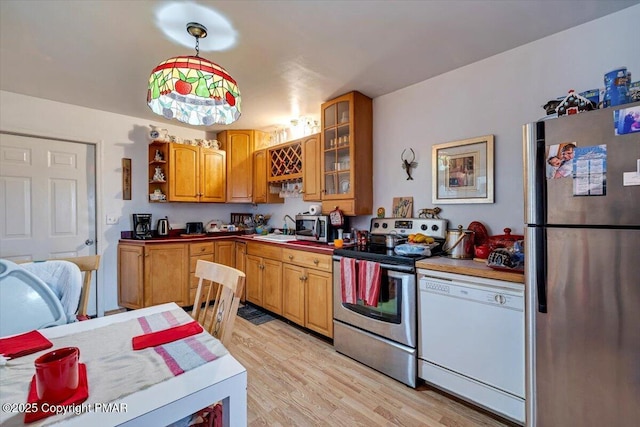 kitchen with stainless steel appliances, a sink, light wood-style floors, open shelves, and glass insert cabinets