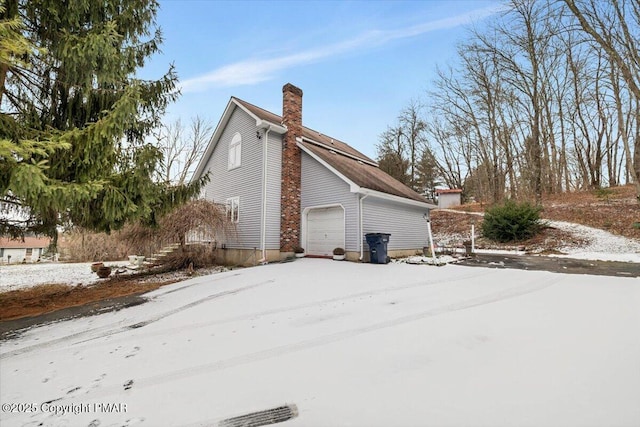 view of snowy exterior featuring a chimney and an attached garage