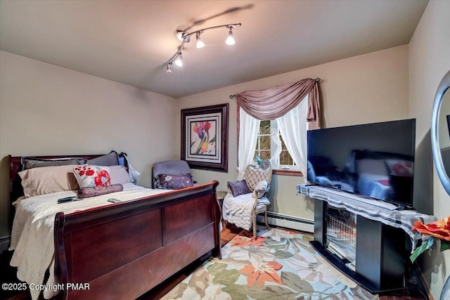 bedroom with rail lighting, baseboard heating, and wood finished floors