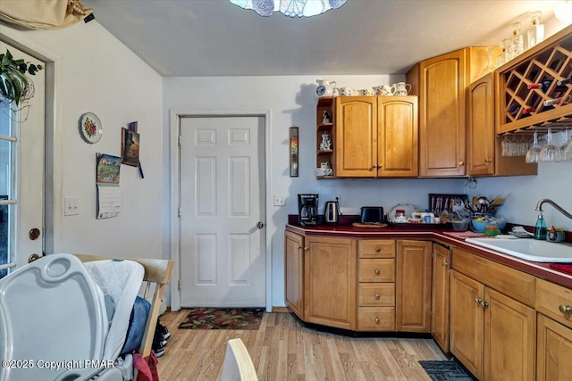 kitchen with a sink, light wood-type flooring, open shelves, brown cabinetry, and dark countertops