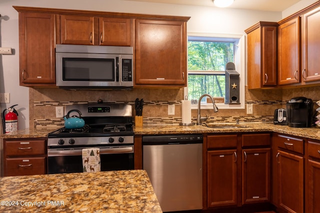 kitchen featuring appliances with stainless steel finishes, a sink, backsplash, and light stone counters