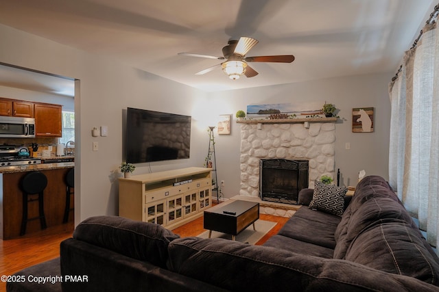 living area featuring a ceiling fan, light wood-type flooring, and a fireplace