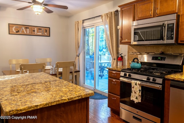 kitchen featuring ceiling fan, stainless steel appliances, dark wood-type flooring, backsplash, and light stone countertops