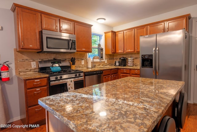 kitchen featuring appliances with stainless steel finishes, brown cabinetry, a sink, and tasteful backsplash