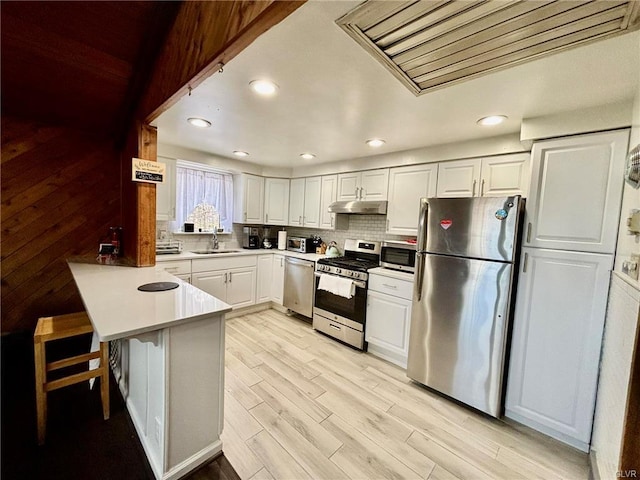 kitchen with under cabinet range hood, decorative backsplash, appliances with stainless steel finishes, and a peninsula