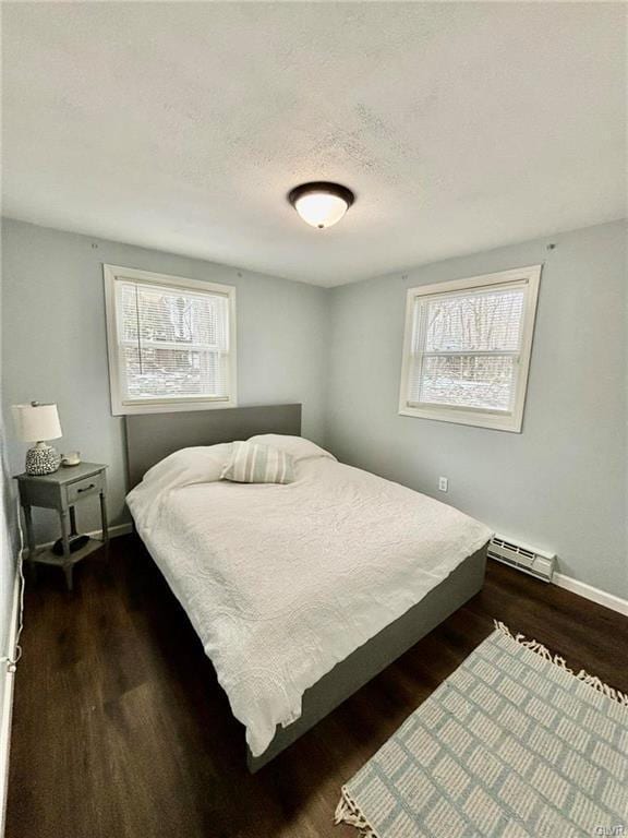 bedroom featuring a baseboard heating unit, multiple windows, wood finished floors, and a textured ceiling