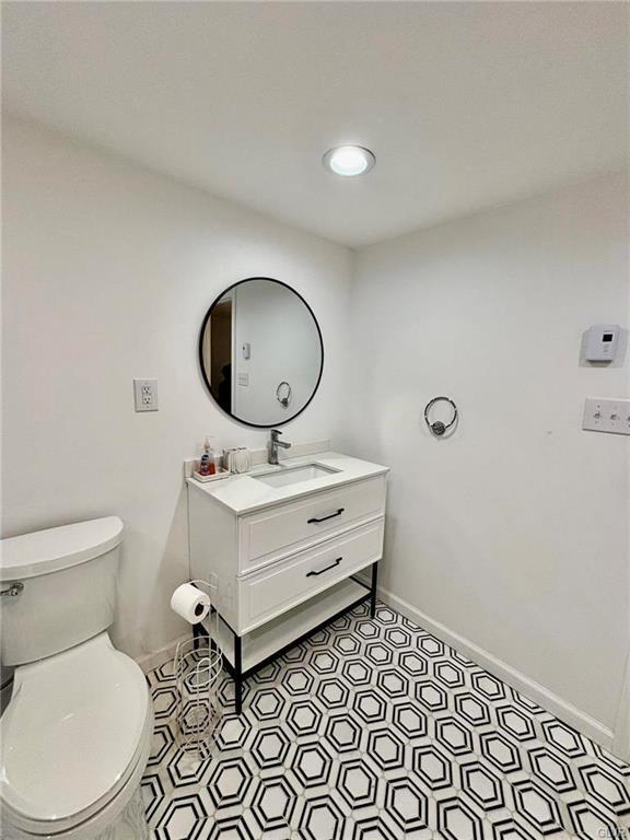 half bathroom with baseboards, toilet, and vanity