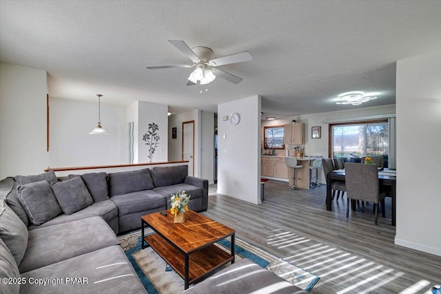 living area with light wood finished floors, a ceiling fan, baseboards, and a textured ceiling