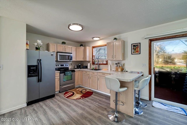 kitchen featuring light countertops, appliances with stainless steel finishes, light brown cabinets, a sink, and a peninsula