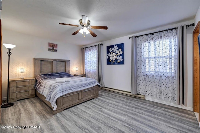 bedroom featuring light wood finished floors, multiple windows, baseboards, and a ceiling fan