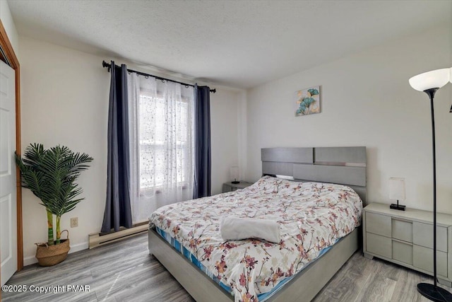 bedroom with light wood-style floors, a baseboard radiator, and a textured ceiling