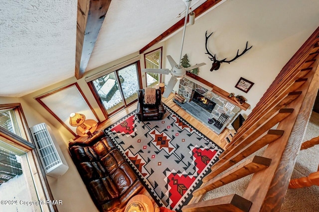 living area featuring a stone fireplace, beamed ceiling, a textured ceiling, and a ceiling fan