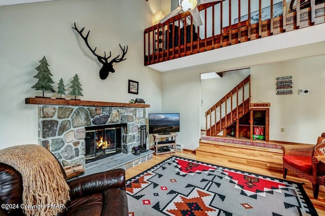 living room with stairs, a stone fireplace, wood finished floors, and a towering ceiling