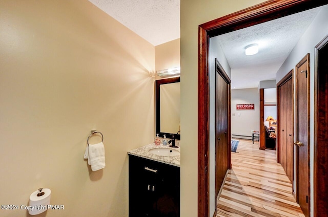 bathroom with baseboard heating, a textured ceiling, vanity, and wood finished floors