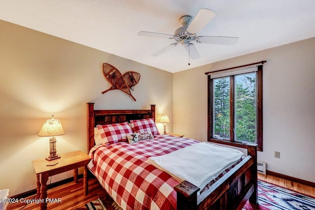 bedroom with a baseboard heating unit, baseboards, wood finished floors, and a ceiling fan