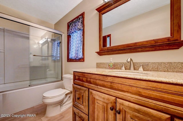 bathroom with toilet, vanity, wood finished floors, enclosed tub / shower combo, and a textured ceiling