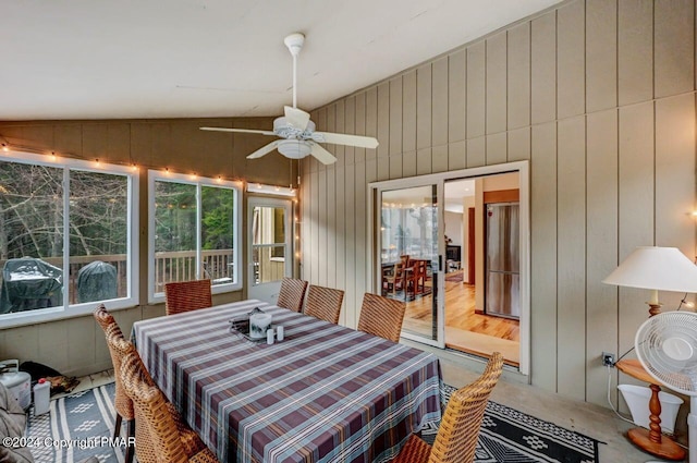 dining space featuring wood walls, a ceiling fan, and vaulted ceiling