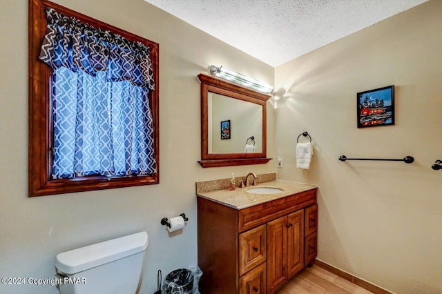 half bath with a textured ceiling, toilet, vanity, and baseboards