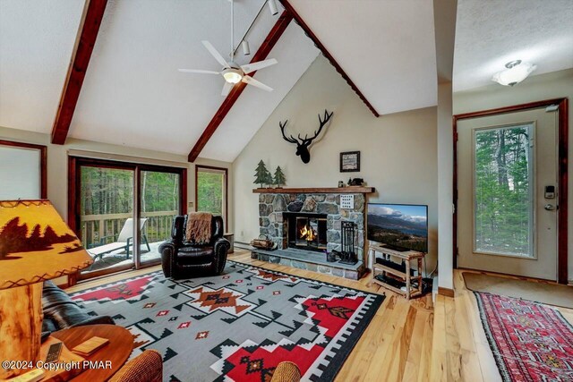 living area with wood finished floors, a ceiling fan, high vaulted ceiling, beam ceiling, and a stone fireplace