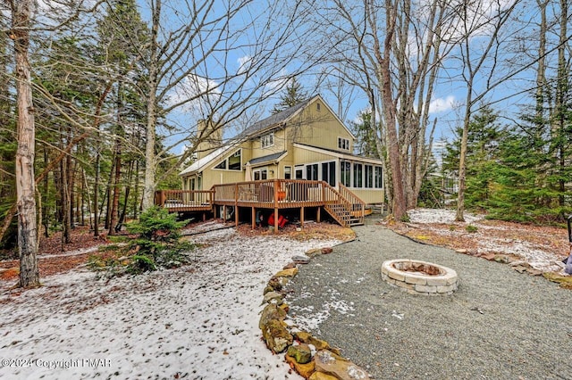 back of property featuring a wooden deck, an outdoor fire pit, and a sunroom