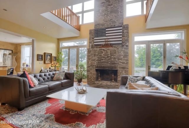 living area with french doors, a stone fireplace, a towering ceiling, and a healthy amount of sunlight