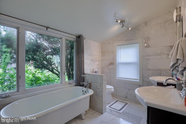 bathroom featuring lofted ceiling, toilet, tile walls, a freestanding bath, and marble finish floor