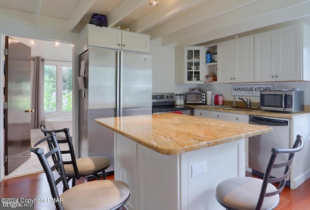 kitchen with appliances with stainless steel finishes, wood finished floors, a sink, white cabinetry, and beam ceiling