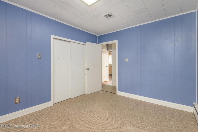 unfurnished bedroom featuring a baseboard heating unit, crown molding, carpet floors, and a closet