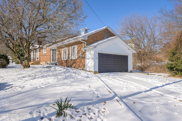 snow covered property with an attached garage and brick siding