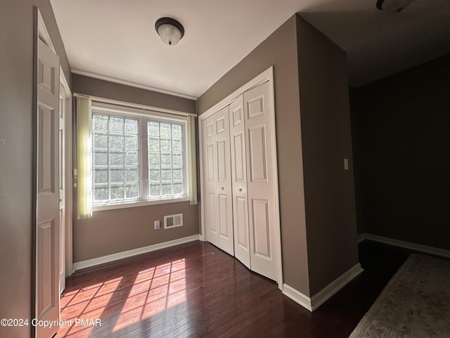 unfurnished bedroom featuring dark wood-style floors, baseboards, visible vents, and a closet