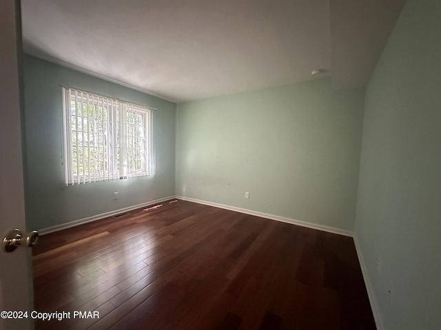 spare room featuring dark wood-style floors, visible vents, and baseboards