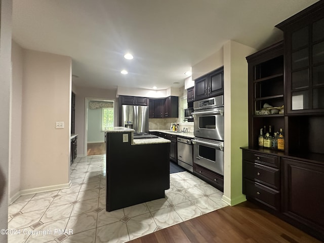 kitchen with baseboards, decorative backsplash, light wood-style flooring, appliances with stainless steel finishes, and a center island