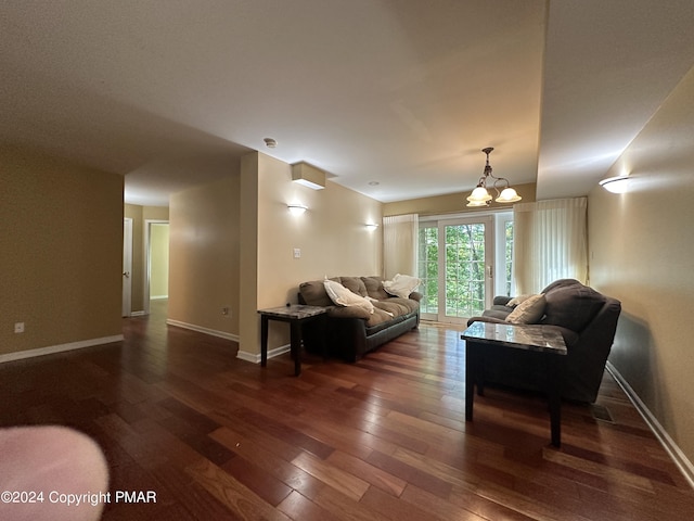 living room featuring dark wood-type flooring, a notable chandelier, and baseboards