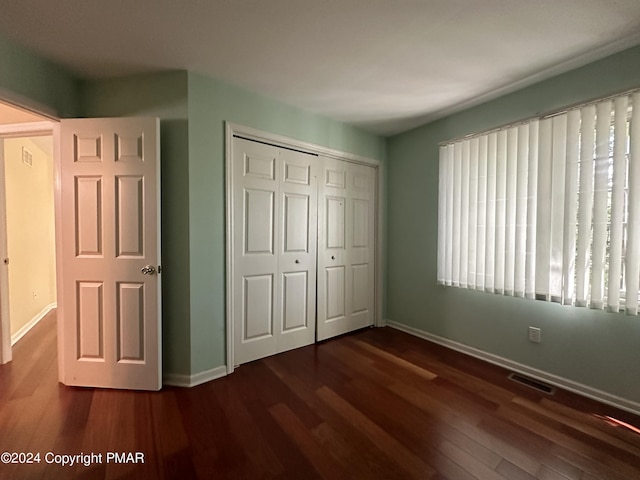 unfurnished bedroom with dark wood-style floors, a closet, visible vents, and baseboards