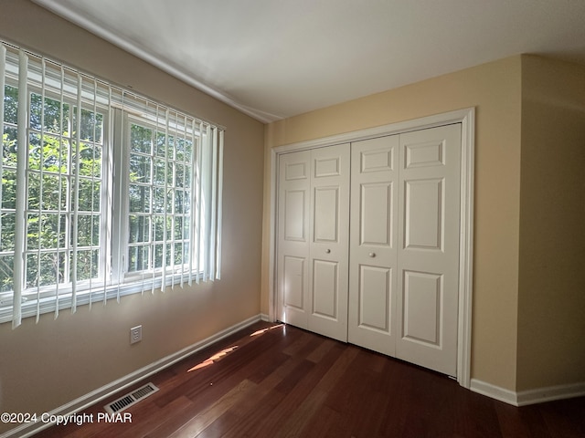 unfurnished bedroom with dark wood-style flooring, a closet, visible vents, and baseboards