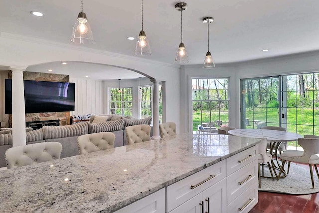 kitchen featuring ornate columns, arched walkways, open floor plan, light stone countertops, and pendant lighting