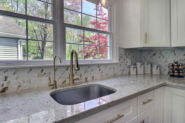 kitchen with a sink, decorative backsplash, white cabinetry, and light stone countertops