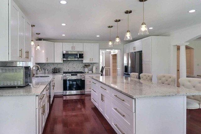 kitchen with appliances with stainless steel finishes, a sink, dark wood-style flooring, white cabinetry, and light stone counters