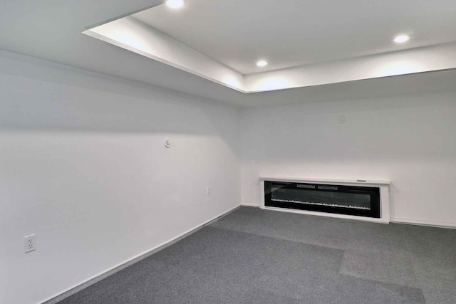 unfurnished living room with a glass covered fireplace, carpet flooring, recessed lighting, baseboards, and a raised ceiling
