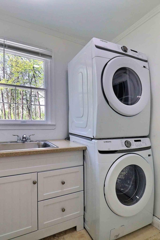 clothes washing area with estacked washer and dryer, crown molding, and cabinet space