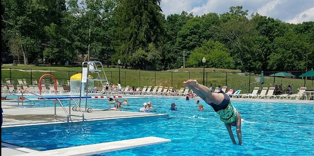 community pool with a yard, a patio area, fence, and a diving board