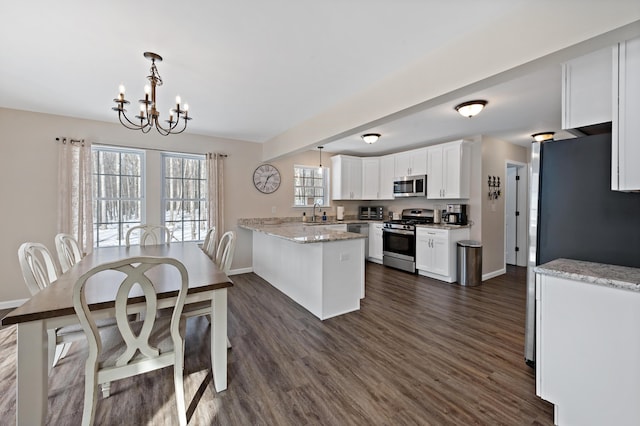 kitchen with dark wood finished floors, appliances with stainless steel finishes, a peninsula, white cabinetry, and a notable chandelier