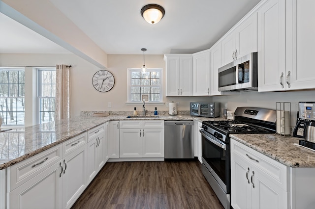 kitchen with dark wood-style floors, appliances with stainless steel finishes, a peninsula, white cabinetry, and a sink