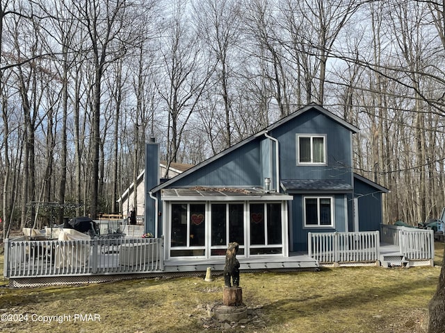 rear view of house featuring a deck, a lawn, a chimney, and a sunroom