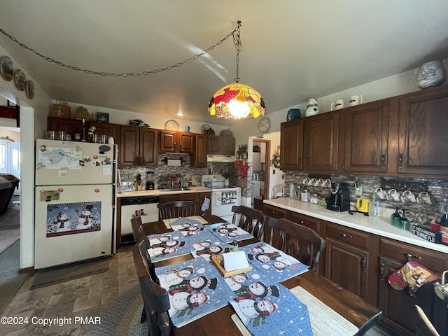 kitchen with white appliances, light countertops, dark brown cabinets, pendant lighting, and backsplash